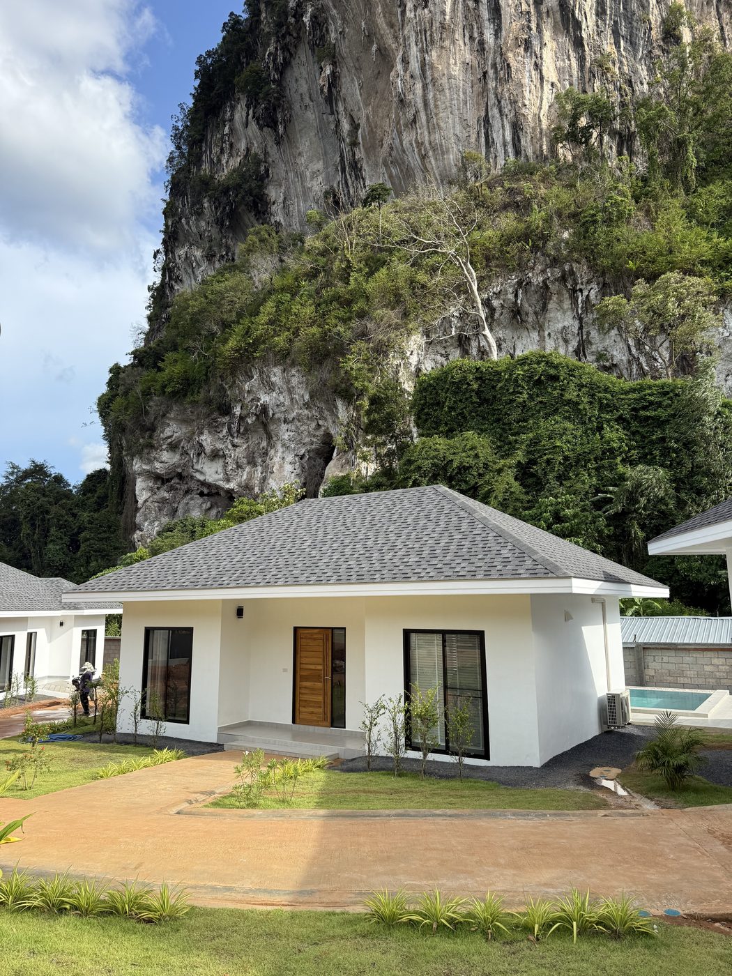 Completed villa with white facade and forecourt in front of a limestone cliff